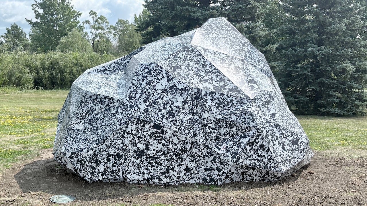 A black and white plastic sculpture resembling a boulder sits in a park.