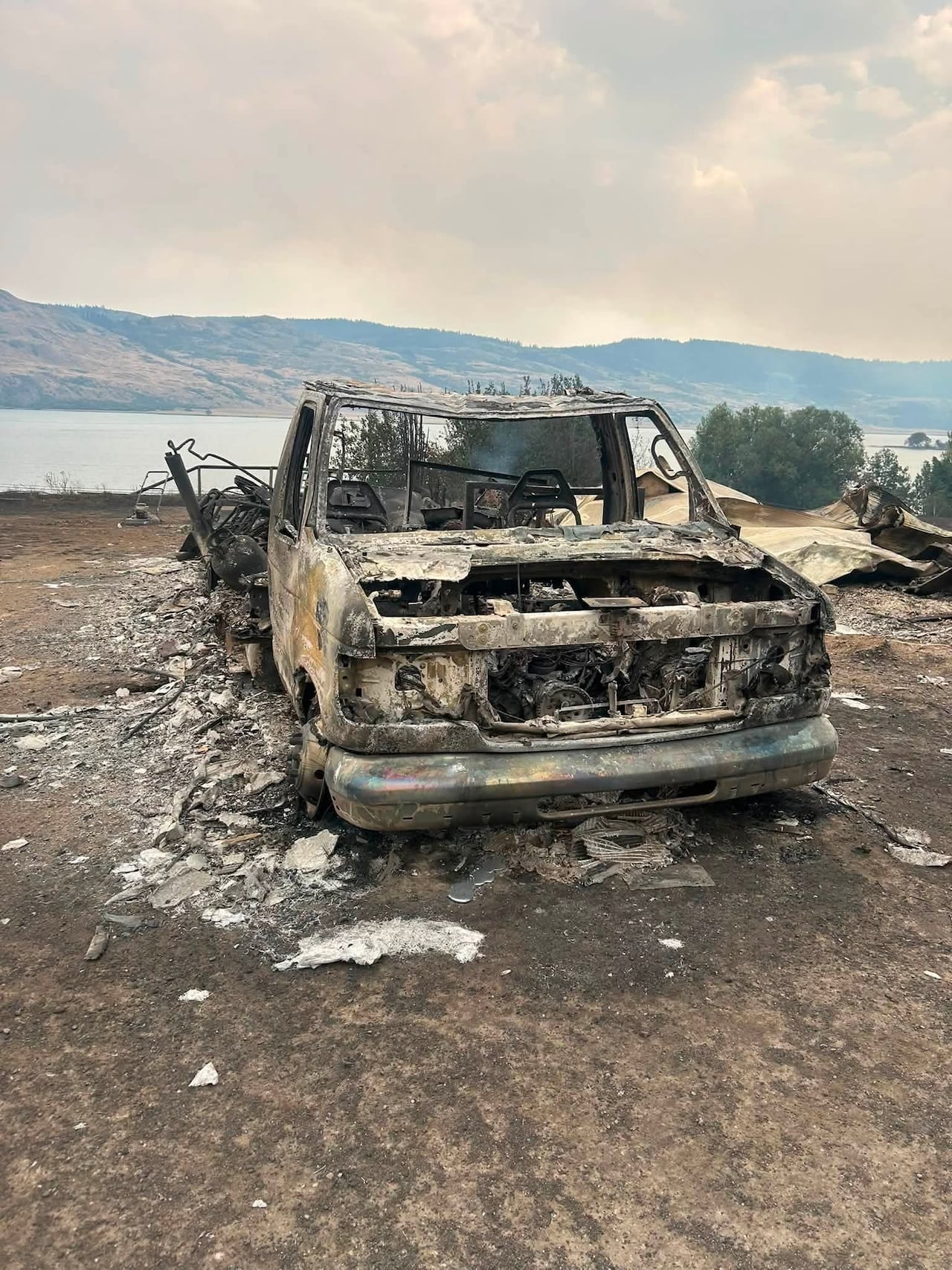 a photo of a burned up truck with Okanagan lake in the background.