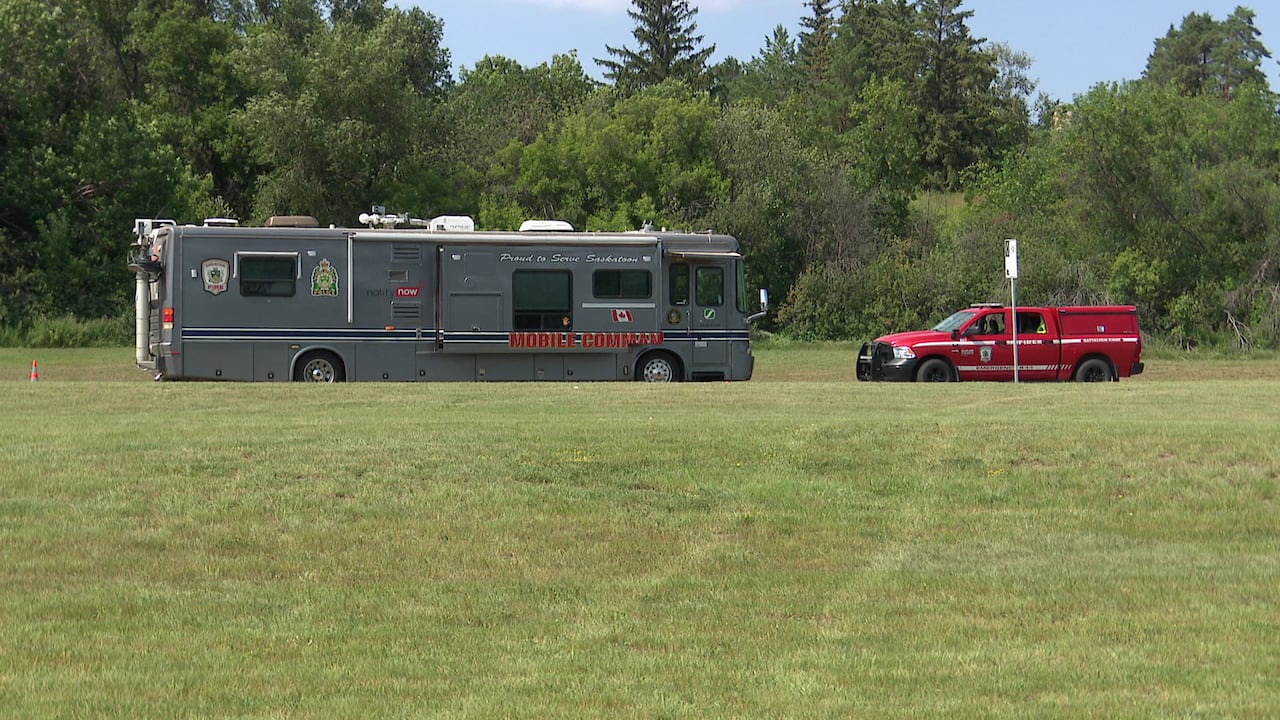A camper van is parked with the words "Mobile Command" on its side. Beside it is a pick-up truck.