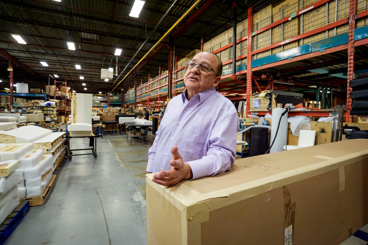 A man leaning on large box in a warehouse filled with furniture, parts on shelves.