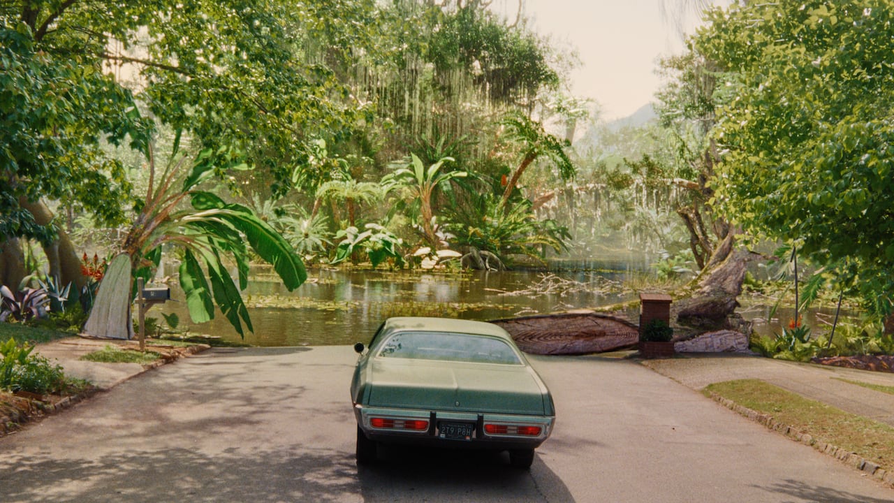 A car is stopped in front of a prehistoric looking lake.