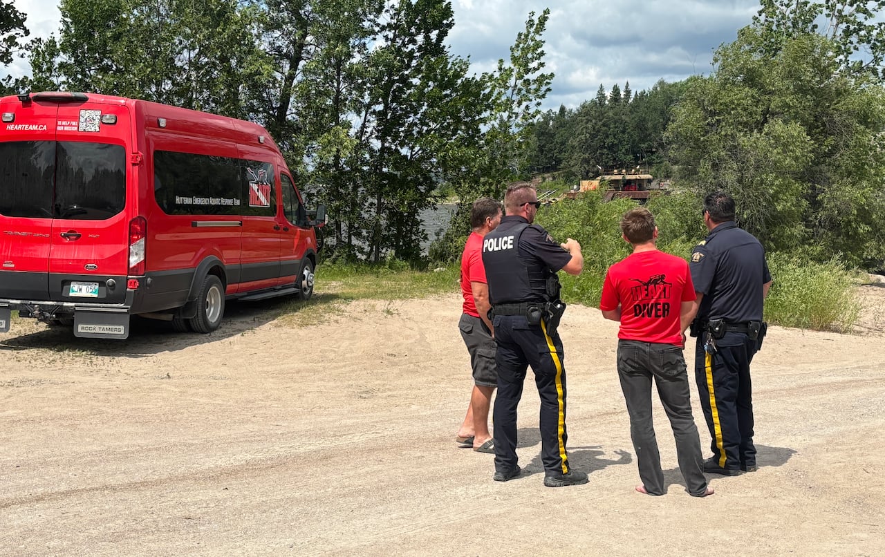 Police officers and rescuers in red speak on the shore of a lake.