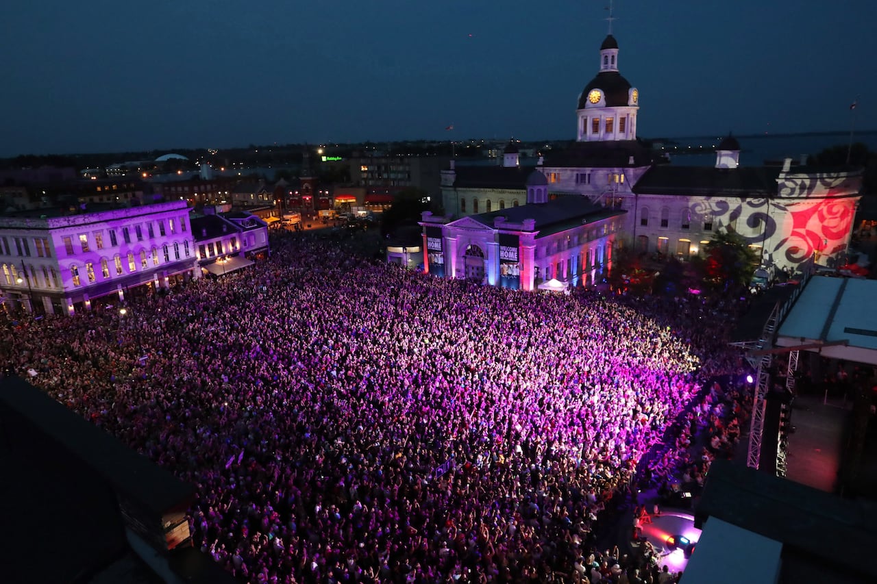 An aerial view of a large crowd standing at night under a pink light.
