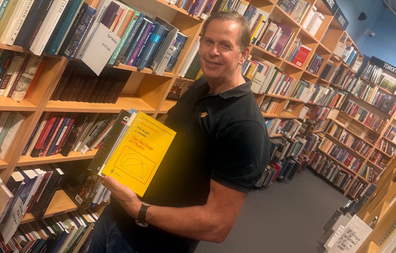 A man stands in a bookstore holding a book.