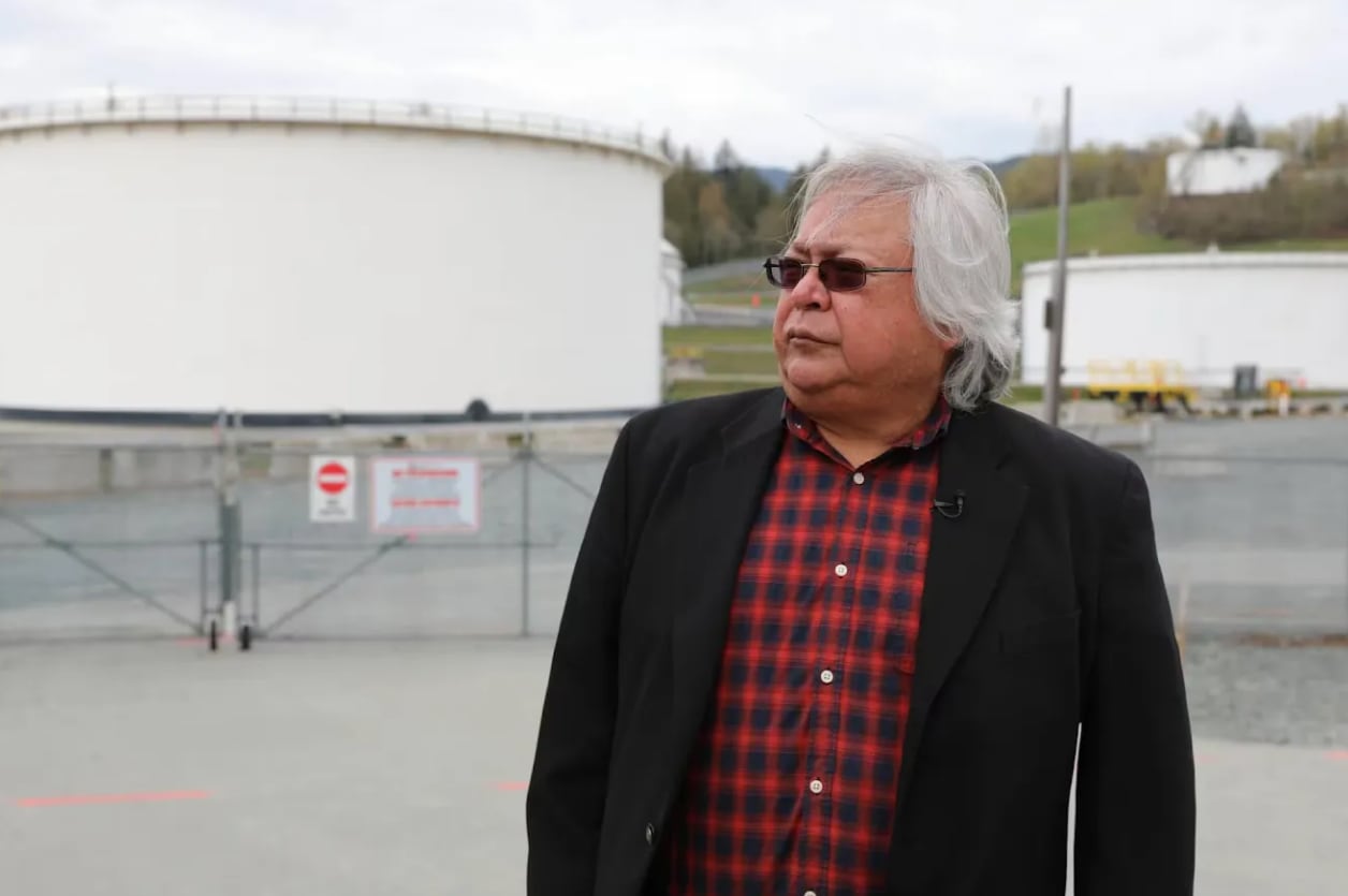 A man stands in front of large industrial tanks.
