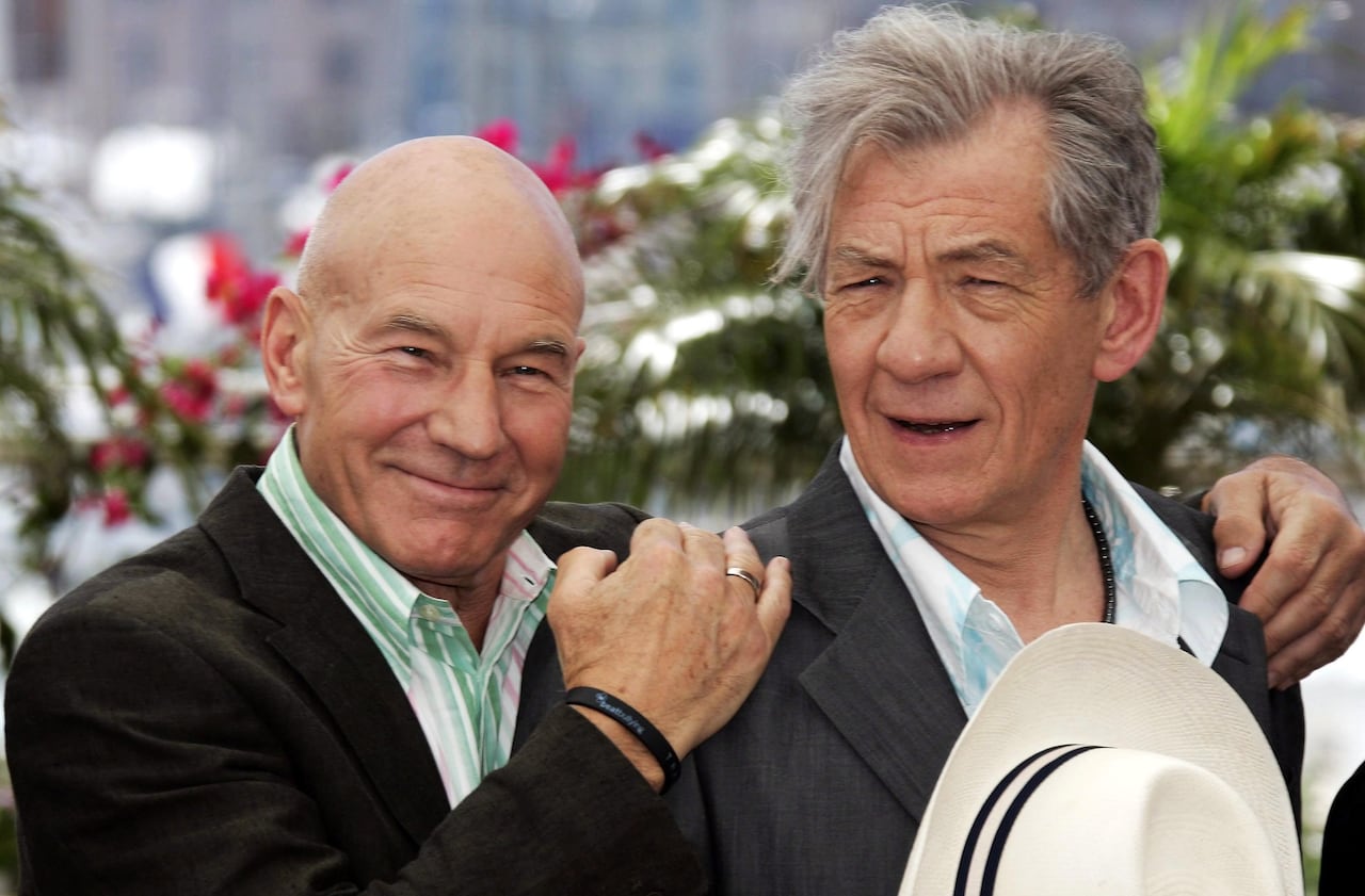 Two men pose together, one holding his hat to his chest and the other holding the man by his shoulders, smiling.