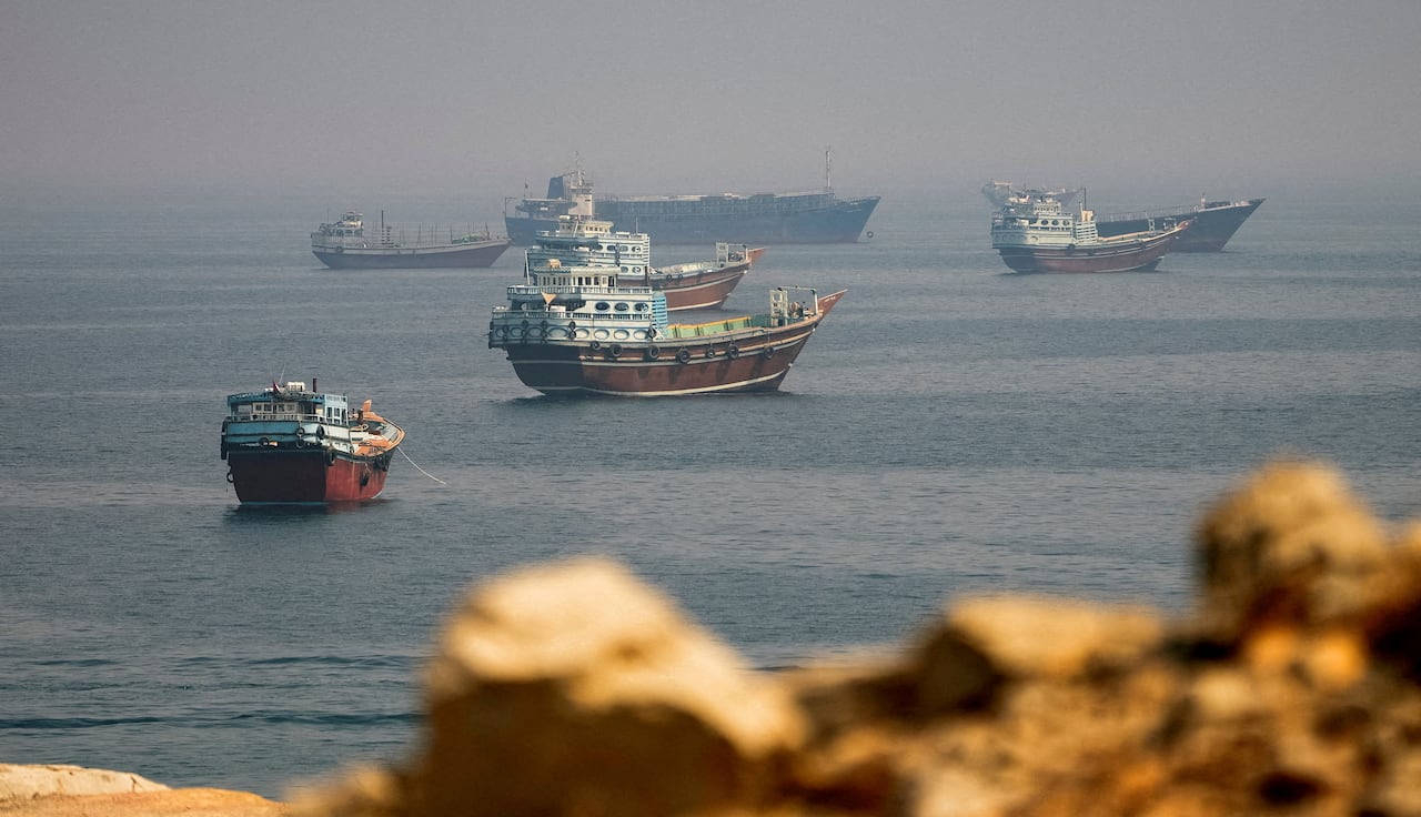 A number of ships are seen on the water. Rocks are in the foreground.