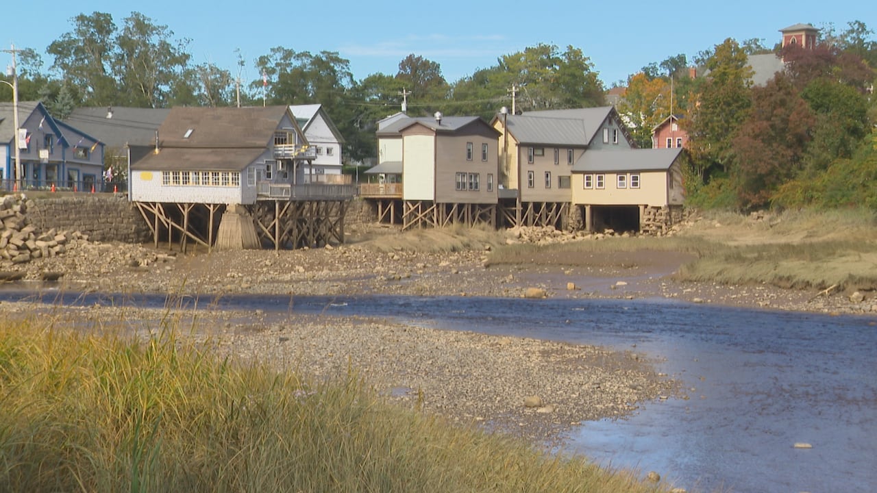 Buildings supported by stilts are seen with a river flowing past them.