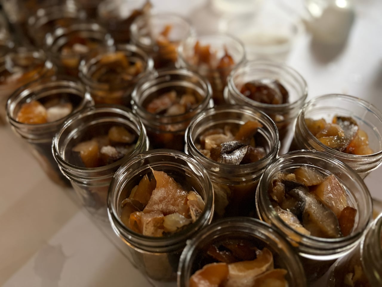 Rows of open glass jars containing pieces of smoked fish sit on a white worktable, ready for canning.