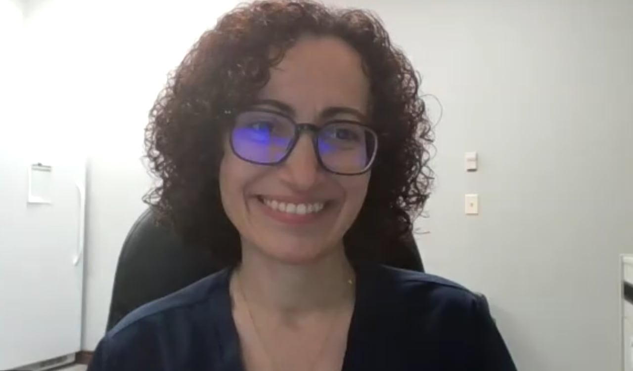 A woman with black chin-length curly hair and glasses smiles