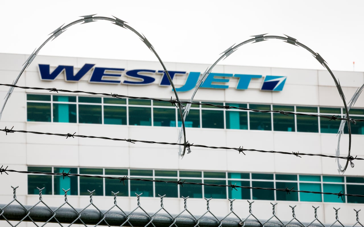 the westjet sign on aa building is pictured behind barbed wire on top of a fence