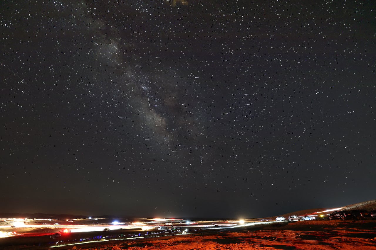 Meteor streaks, stars, the Milky Way seen in the night sky in a desert.