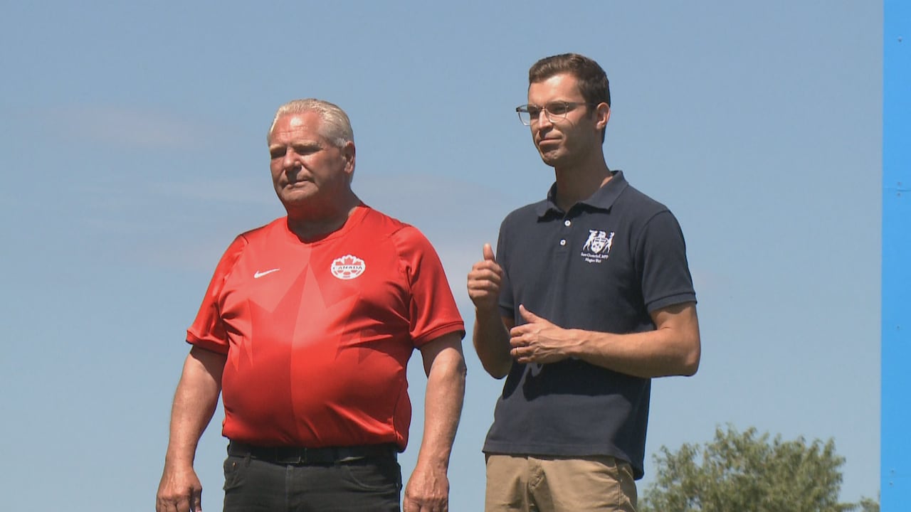 Man in Canada Soccer jersey standing beside another man in polo