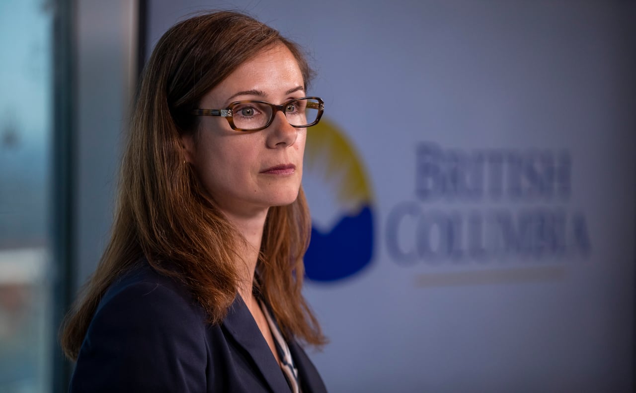 A white woman with brown hair speaks in front of a banner marked 'British Columbia'.