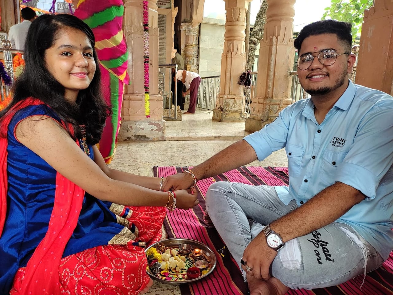 A woman sitting across from a man, tying him a thread.