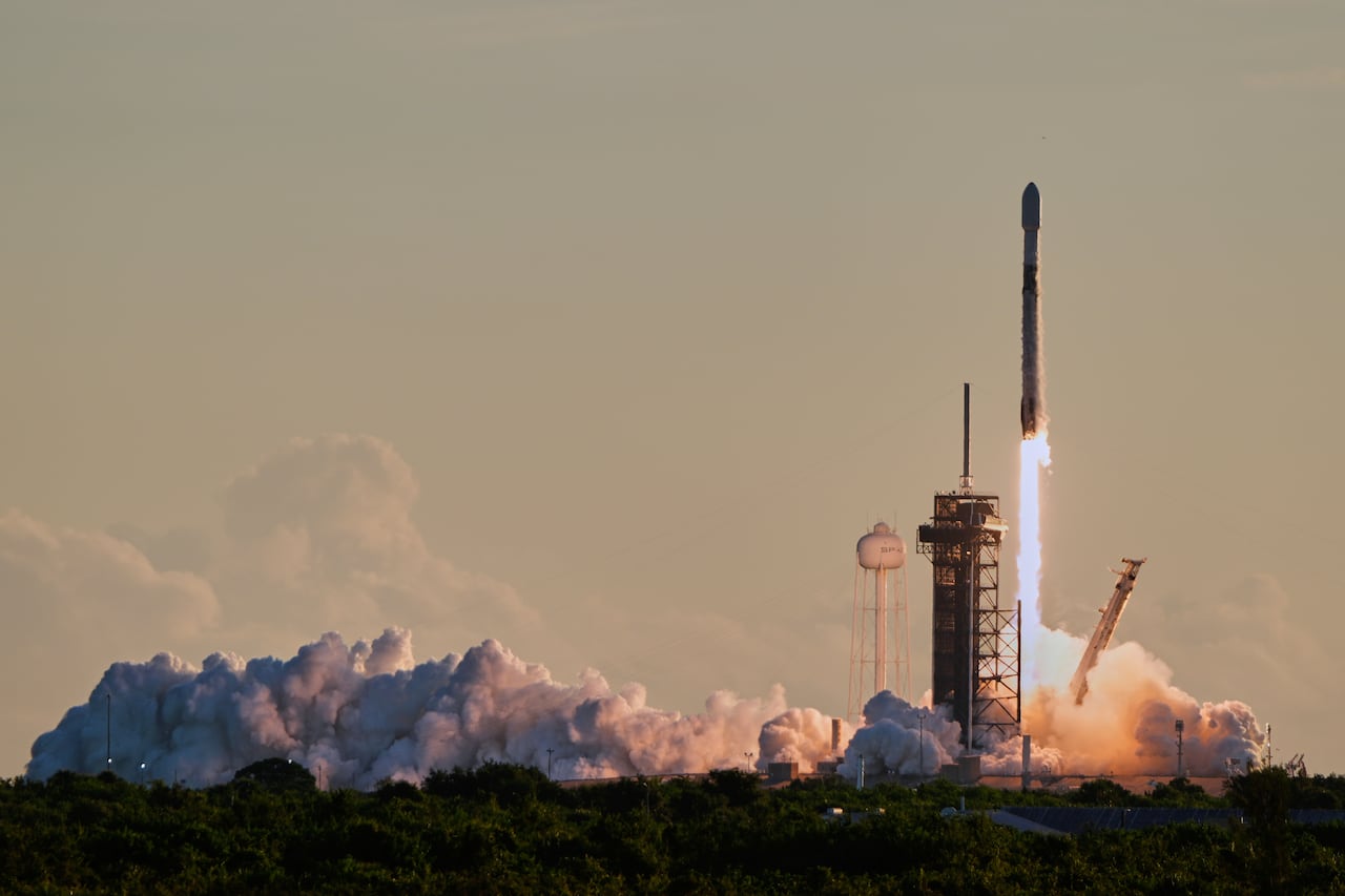 a rocket blasts off from the launchpad in a plume of vapour against an evening sky