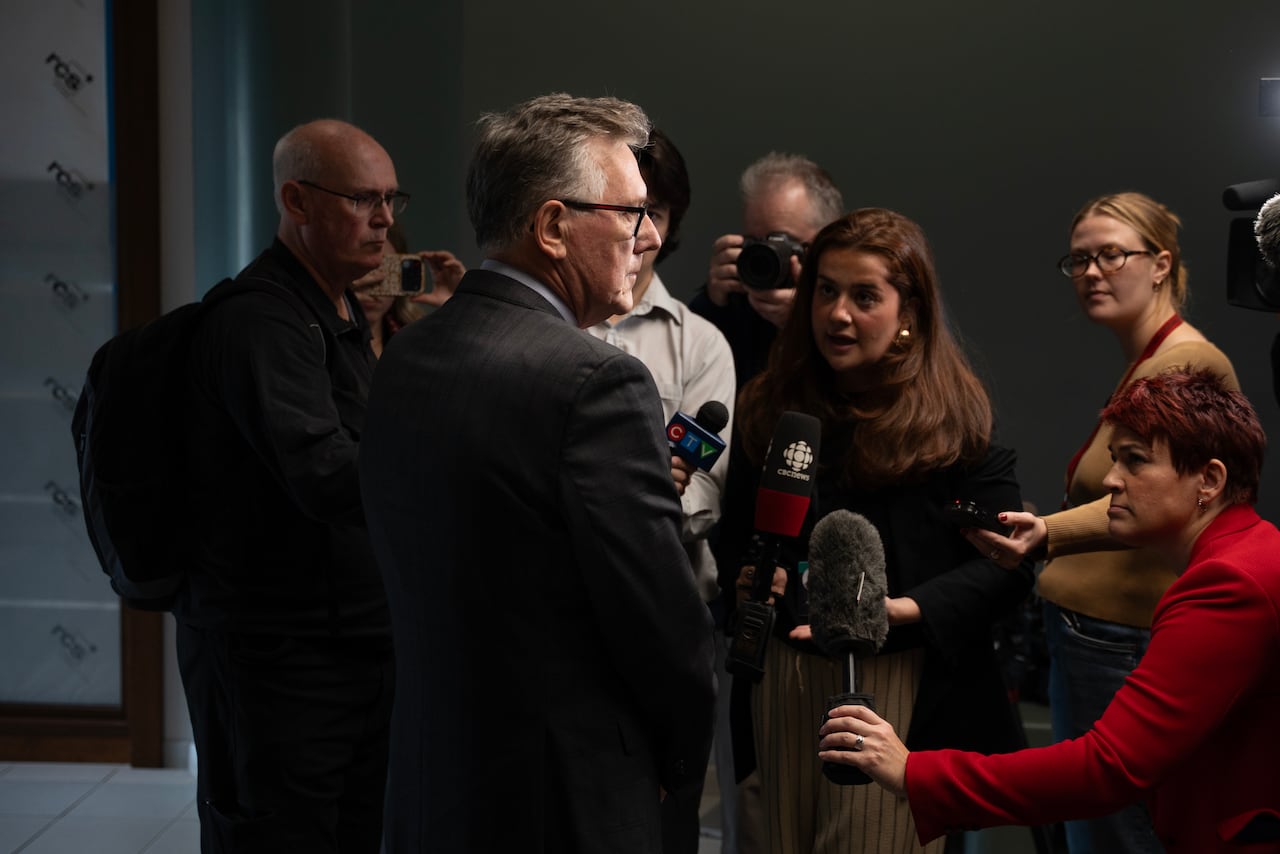 A man in a suit stands in front of reporters holding microphones.