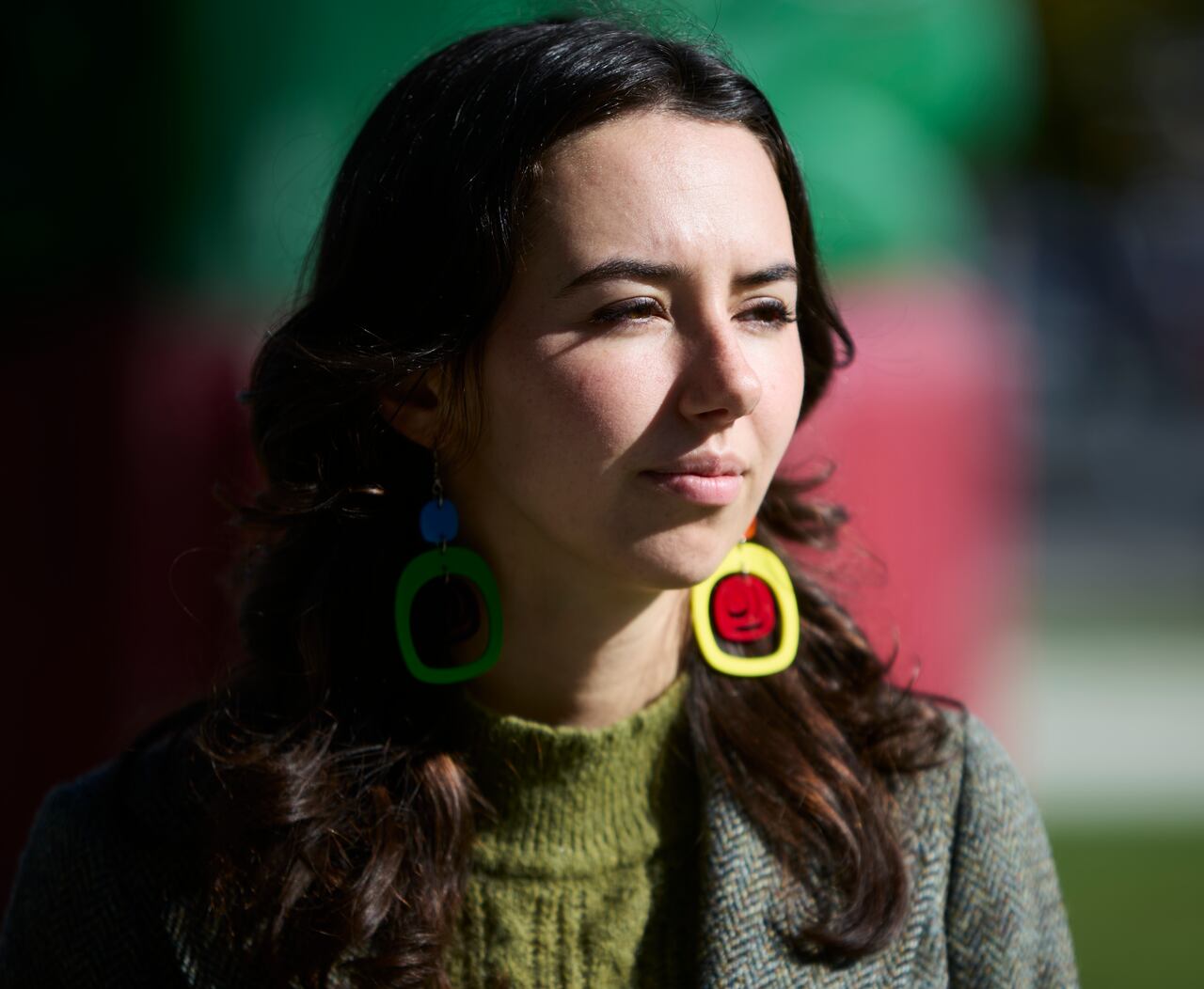 Emily Lowan, a woman with large earrings and wearing a green sweater, is seen in profile.