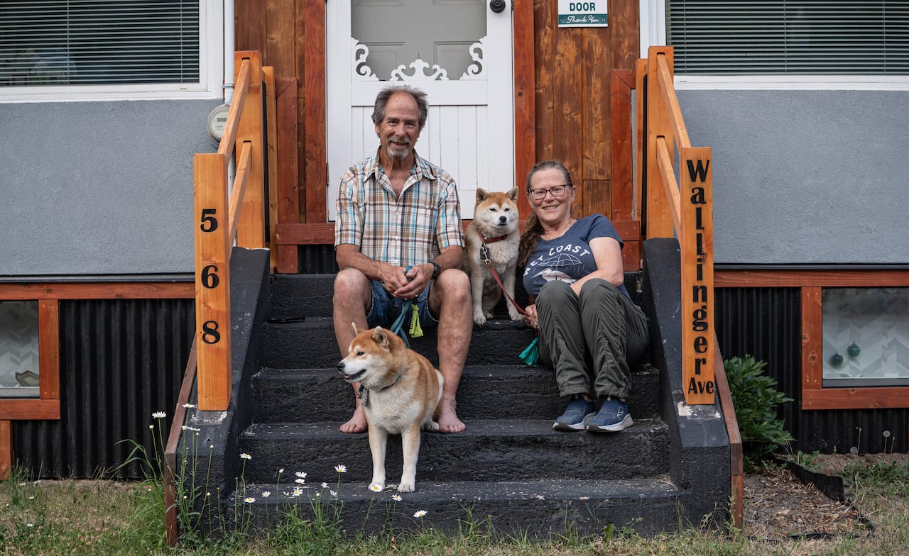 A middle-aged couple sit on the front-step of a home with two dogs.