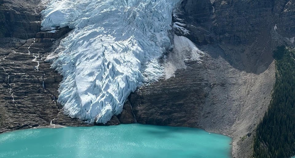 An image of a glacier on a mountain next to a turquoise lake.