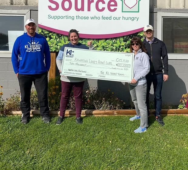 Screenshot of several people holding a large cheque outside a food bank
