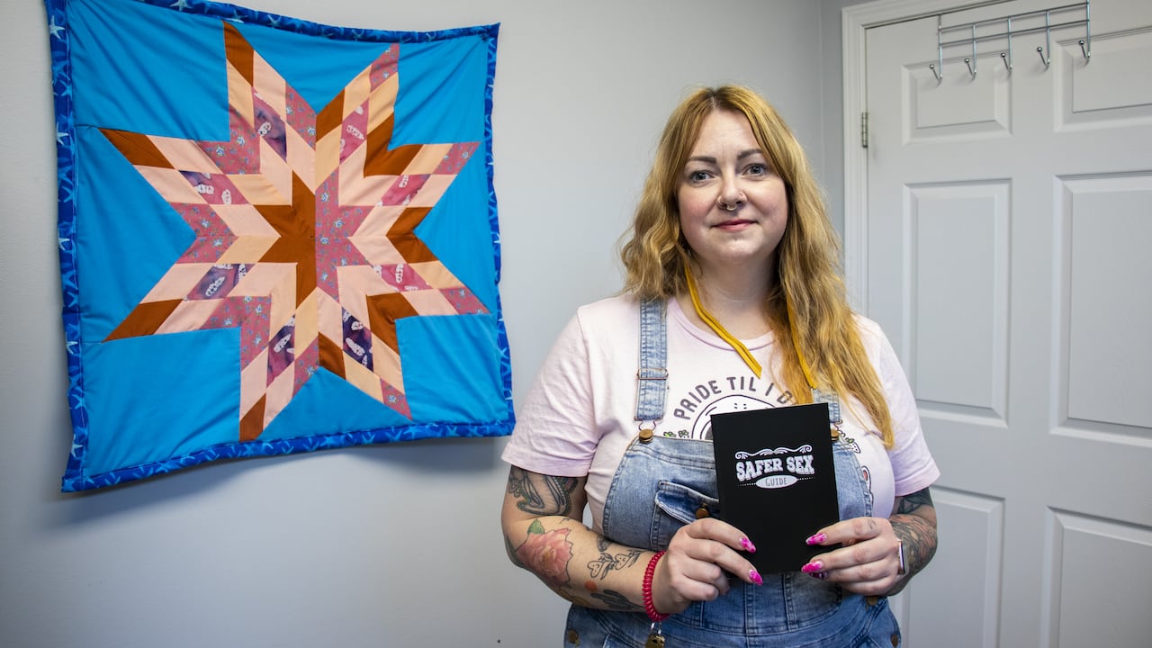 A woman holds a book that says Safer Sex Guide