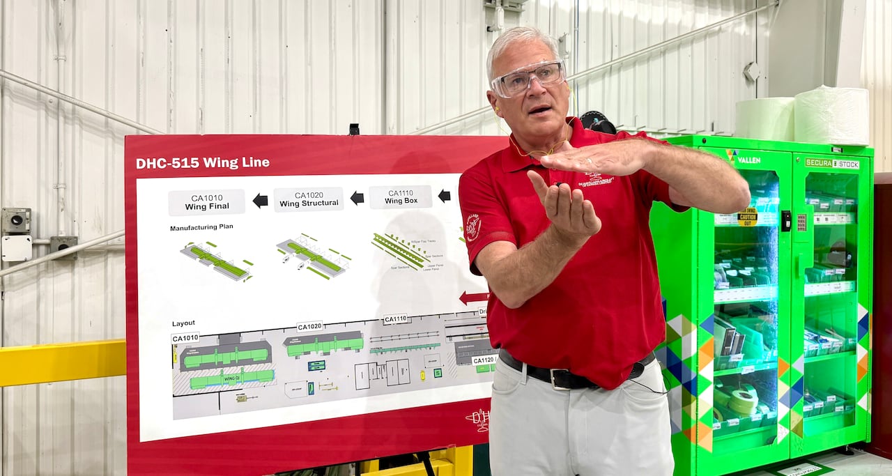The executive gestures with his hands in from of a display showing how the wings of the aircraft are assembled.