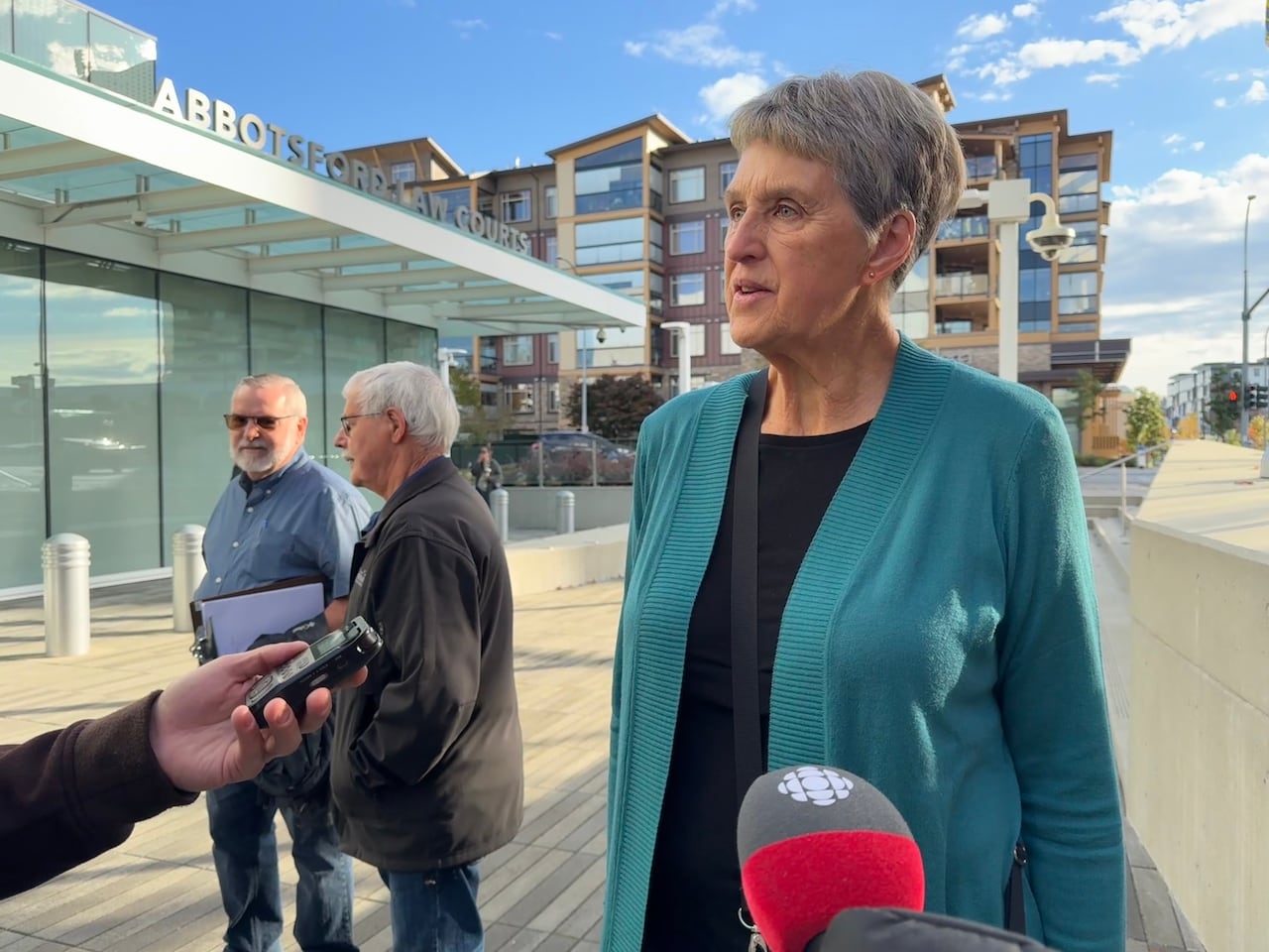 woman in teal cardigan and short grey hair speaks in front of abbotsford law courts