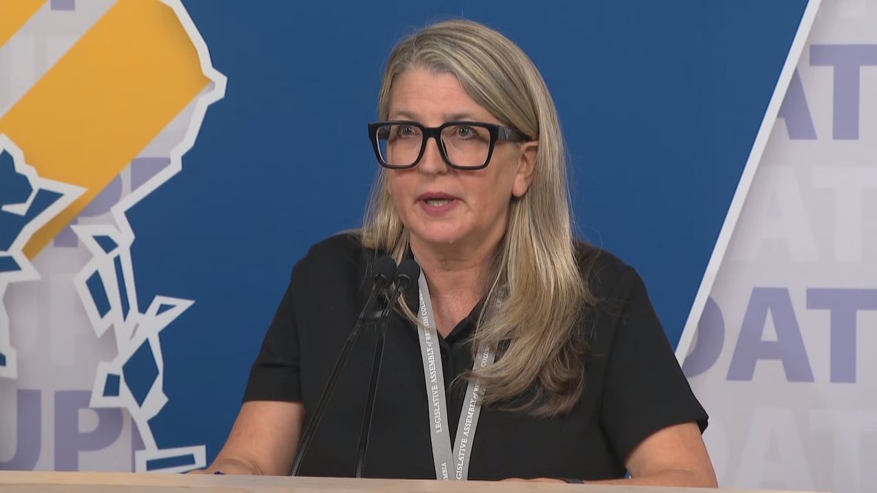 一名金发佩戴黑框眼镜的女士正对着麦克风讲话