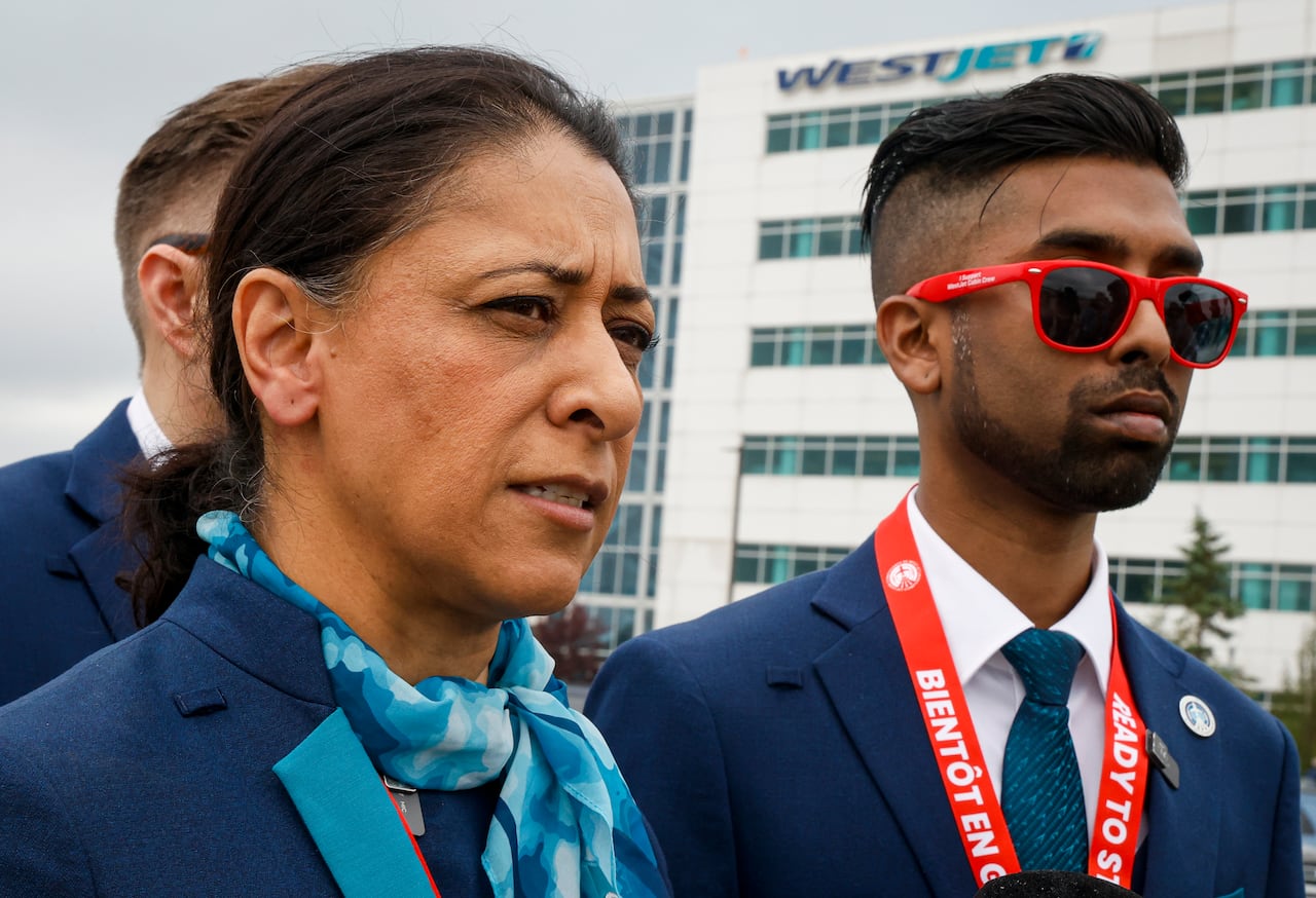 A woman and man in flight attendant uniforms stand in front of the WestJet building with picket signs on.