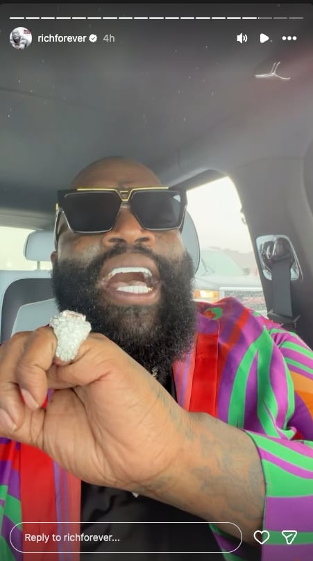 man in colourful jacket, sunglasses and very large ring talks to his phone camera in a car.