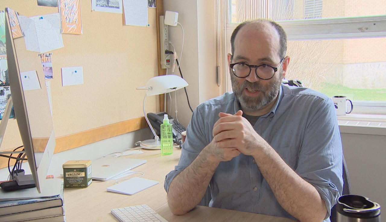 Man with blue shirt and wearing glasses is sitting in his office.