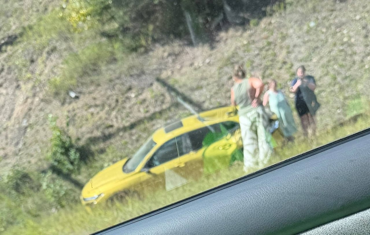 A yellow vehicle crashed on the side of the road with people clustered around it.