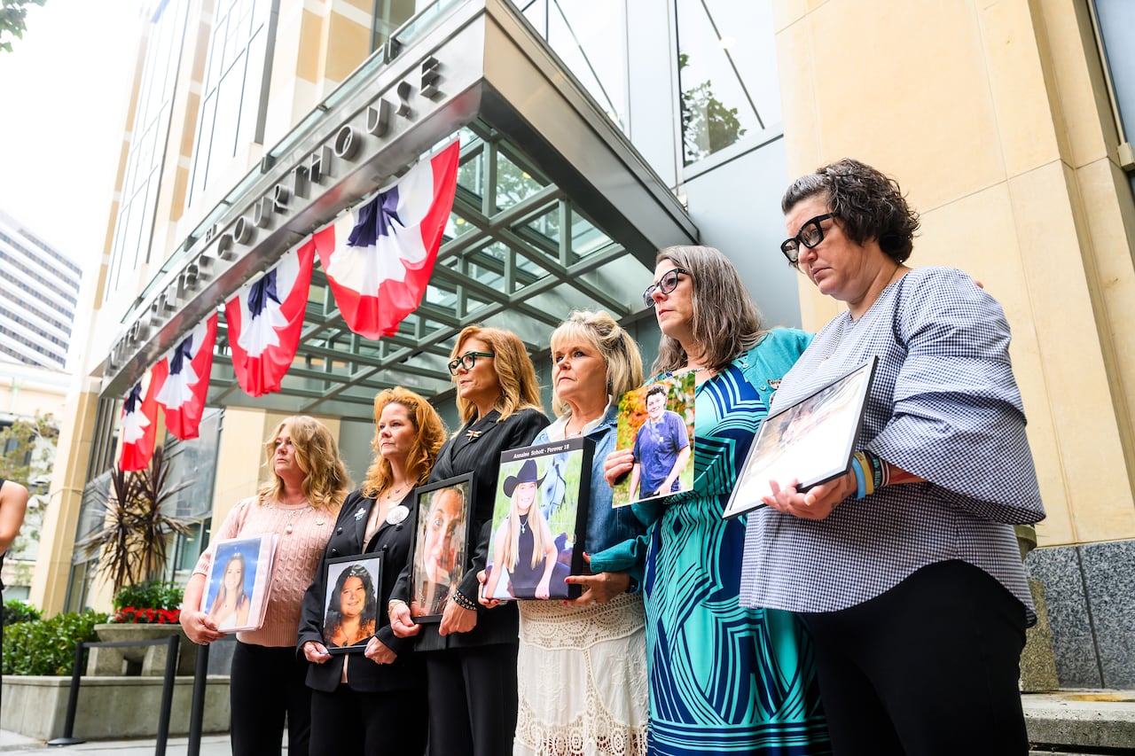 six women standing in a line hold portraits of young people outside a court building