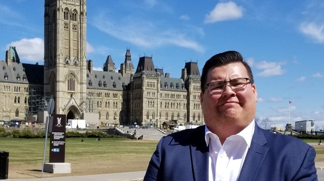 Man in blue suit stands in front of the Parliament buildings.