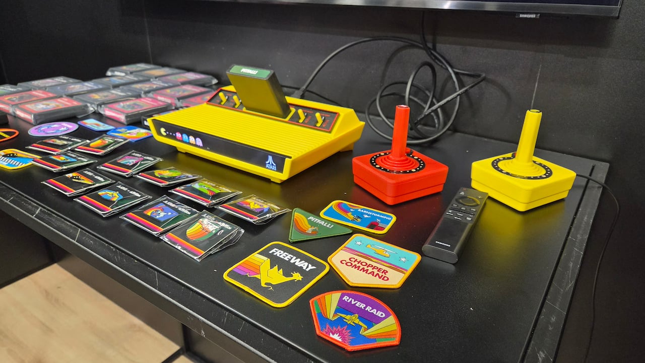 A bright yellow atari console is seen on a table along with other video game accessories and merchandise.