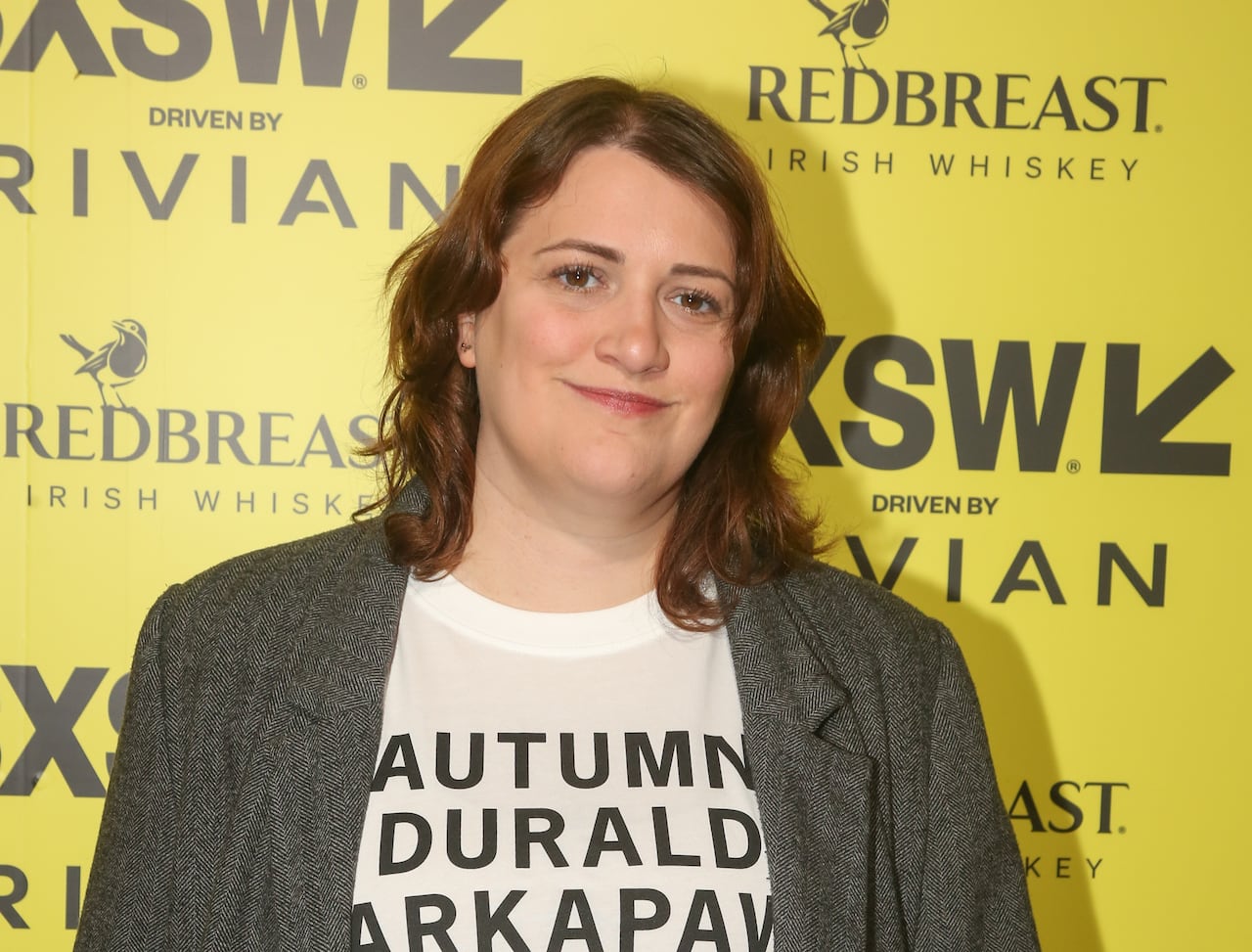 A woman in a jacket and a shirt in front of a promotional backdrop for South by Southwest Film Festival.