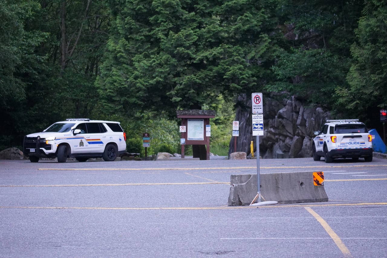 Two RCMP vehicles are parked near the entrance to a forested parking area.