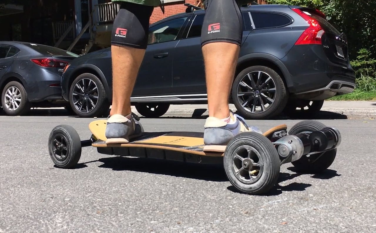 A person's legs are seen on a skateboard with electronics hooked up to the back
