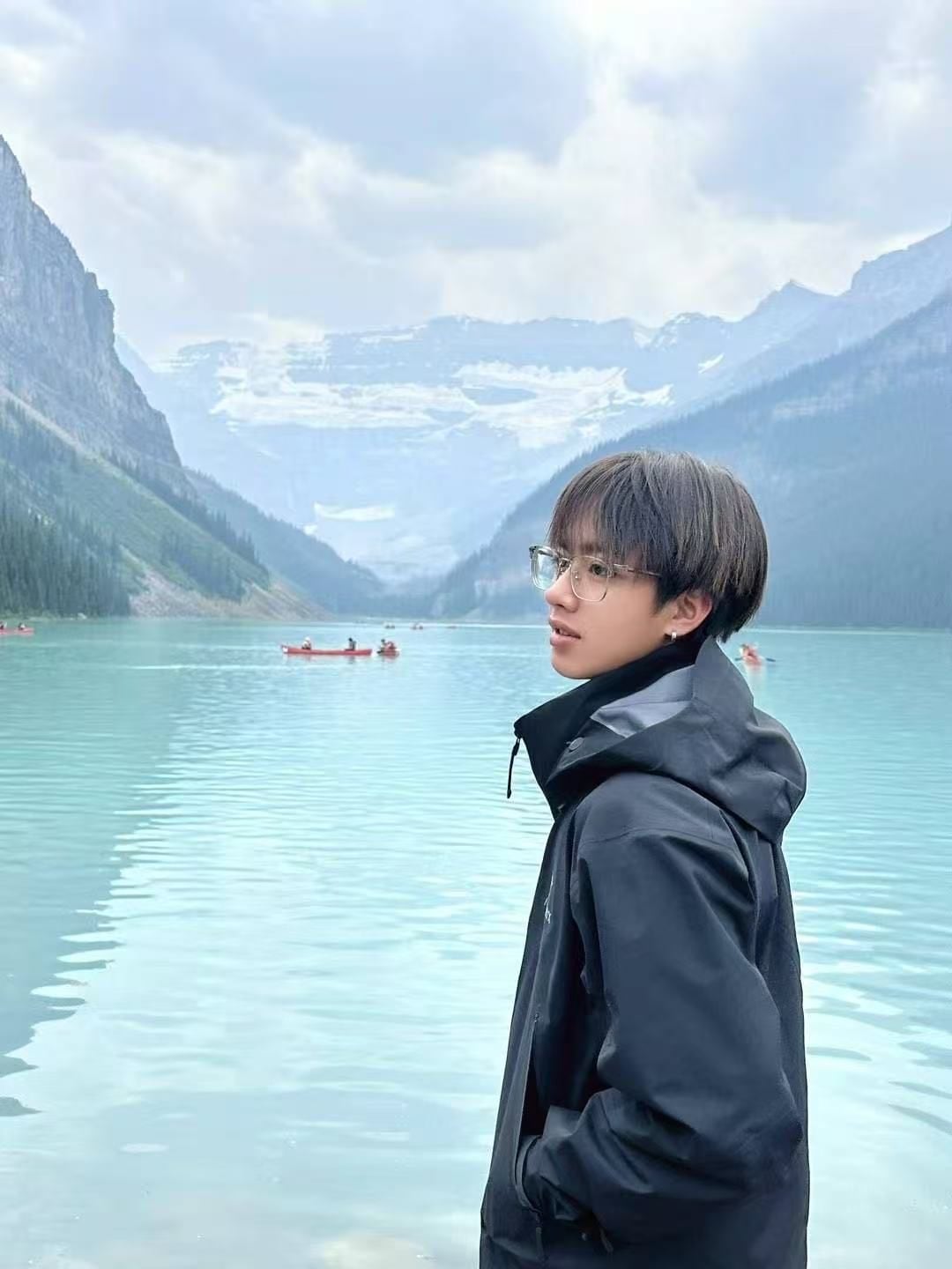 A young Chinese man wearing glasses is seen from behind, a profile of his face turning left; in front of him, views of the mountains.