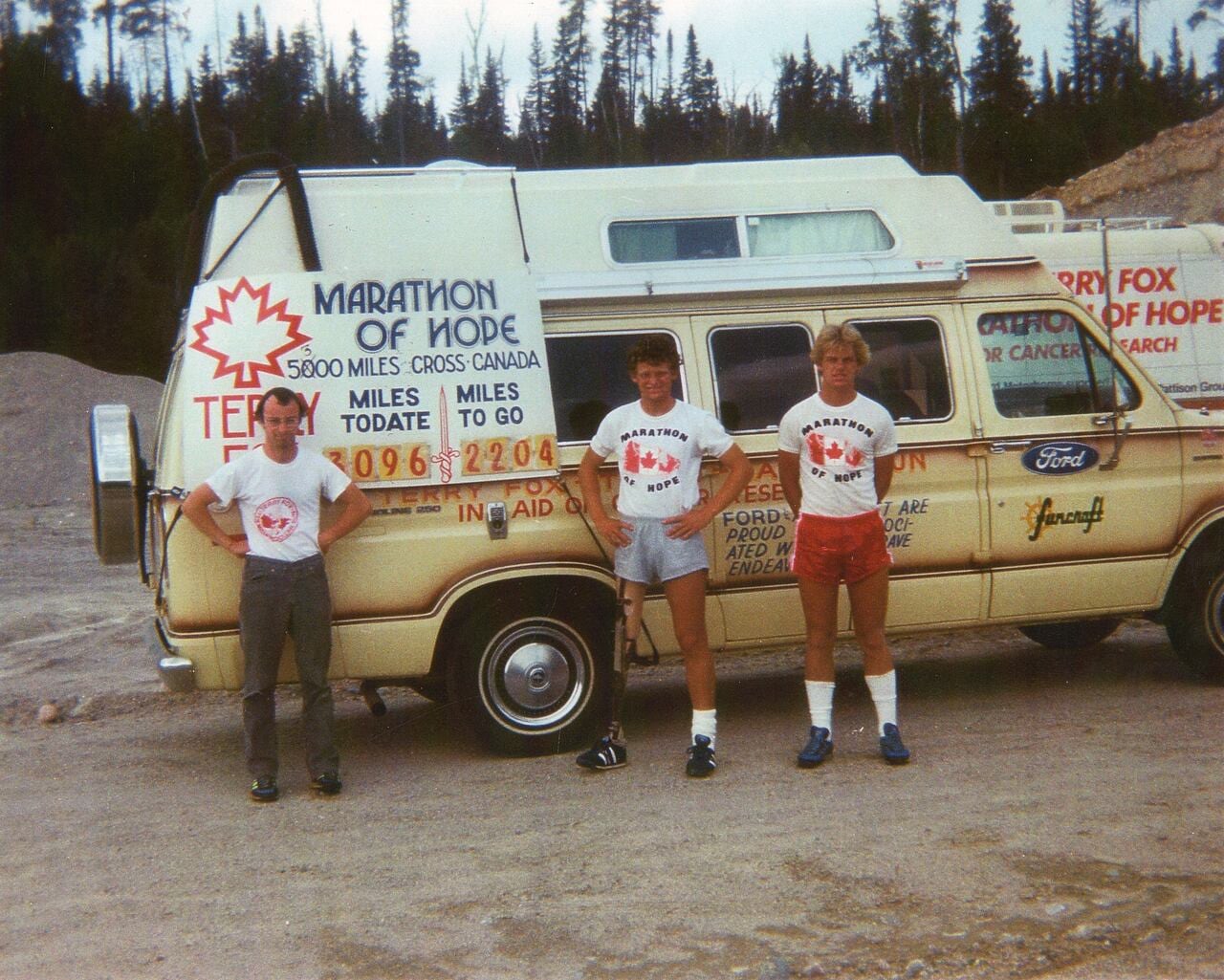 Three men stand in front of van.