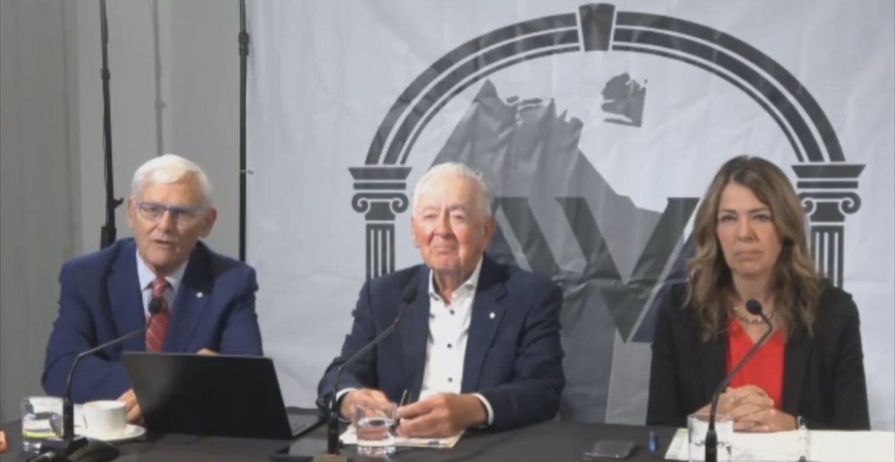 three people at a conference table with a partial conference logo behind them.