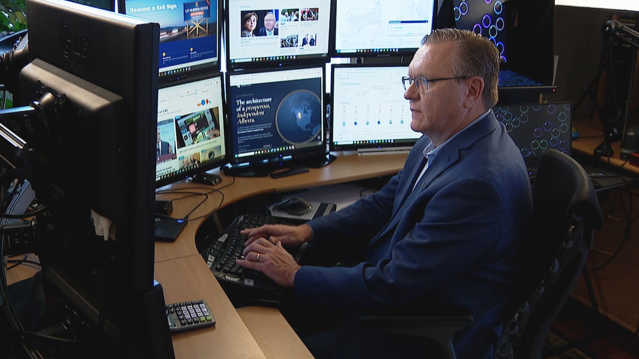A man sits behind a series of computer screens.