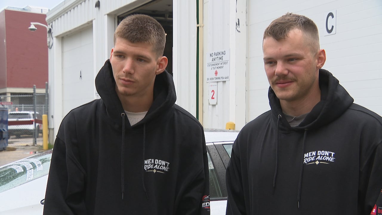 Two men in black hooded sweatshirts stand beside one another outside.