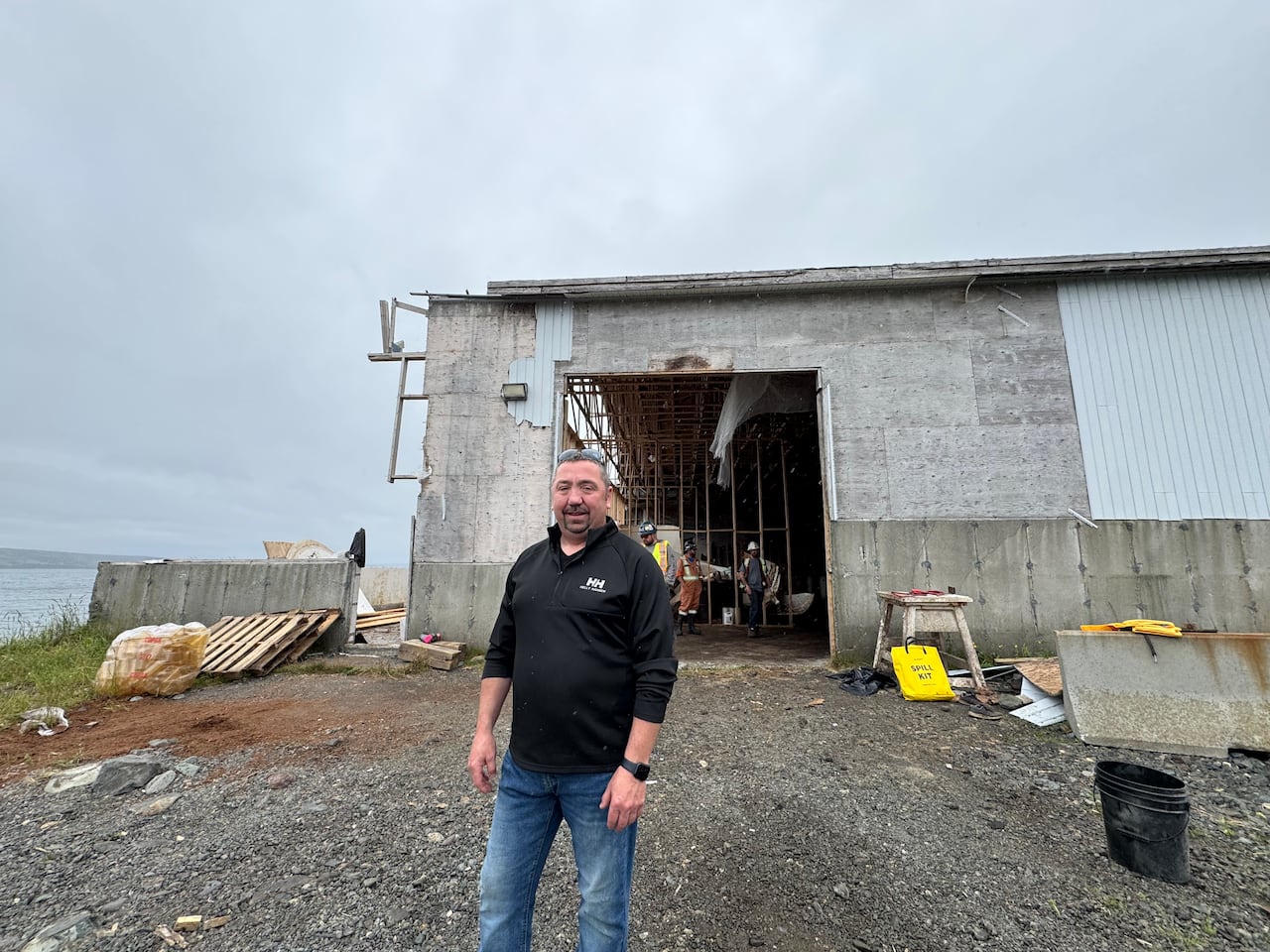 A smiling man stands in front of a worn-down fish sauce plant building.