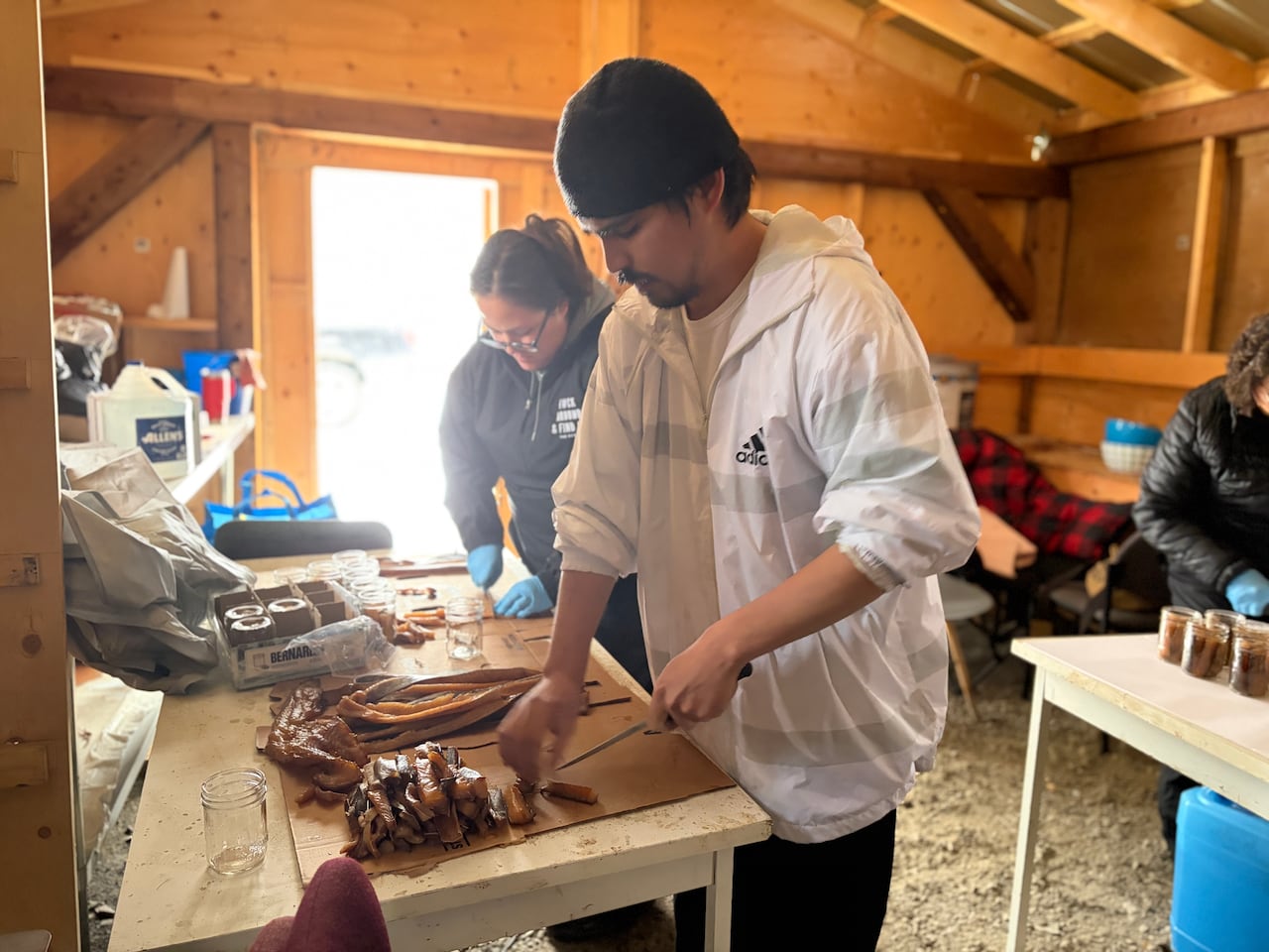 Jordan Cote-Germain, wearing a white jacket and black hat, cuts smoked fish on a table as others work around him.