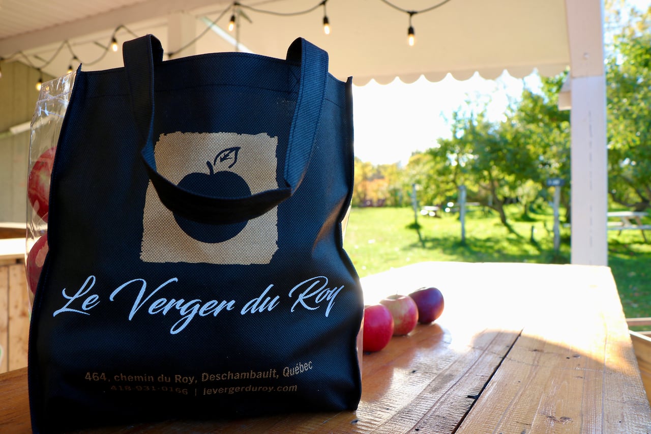 A bag filled with apples on an outside table. The bag is branded "Le Verger du Roy".