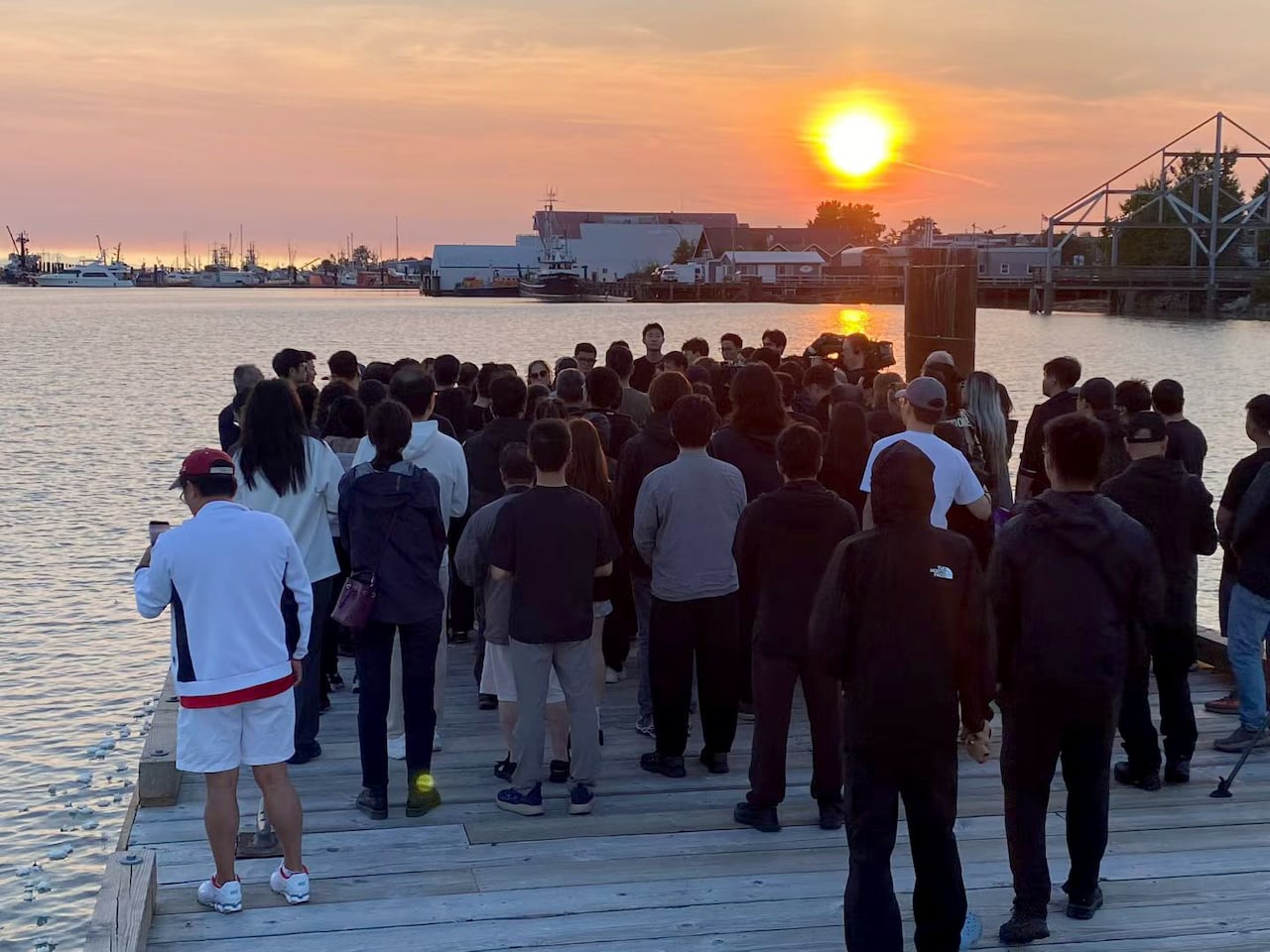 A group of people gather on a dock over the water at sunset.