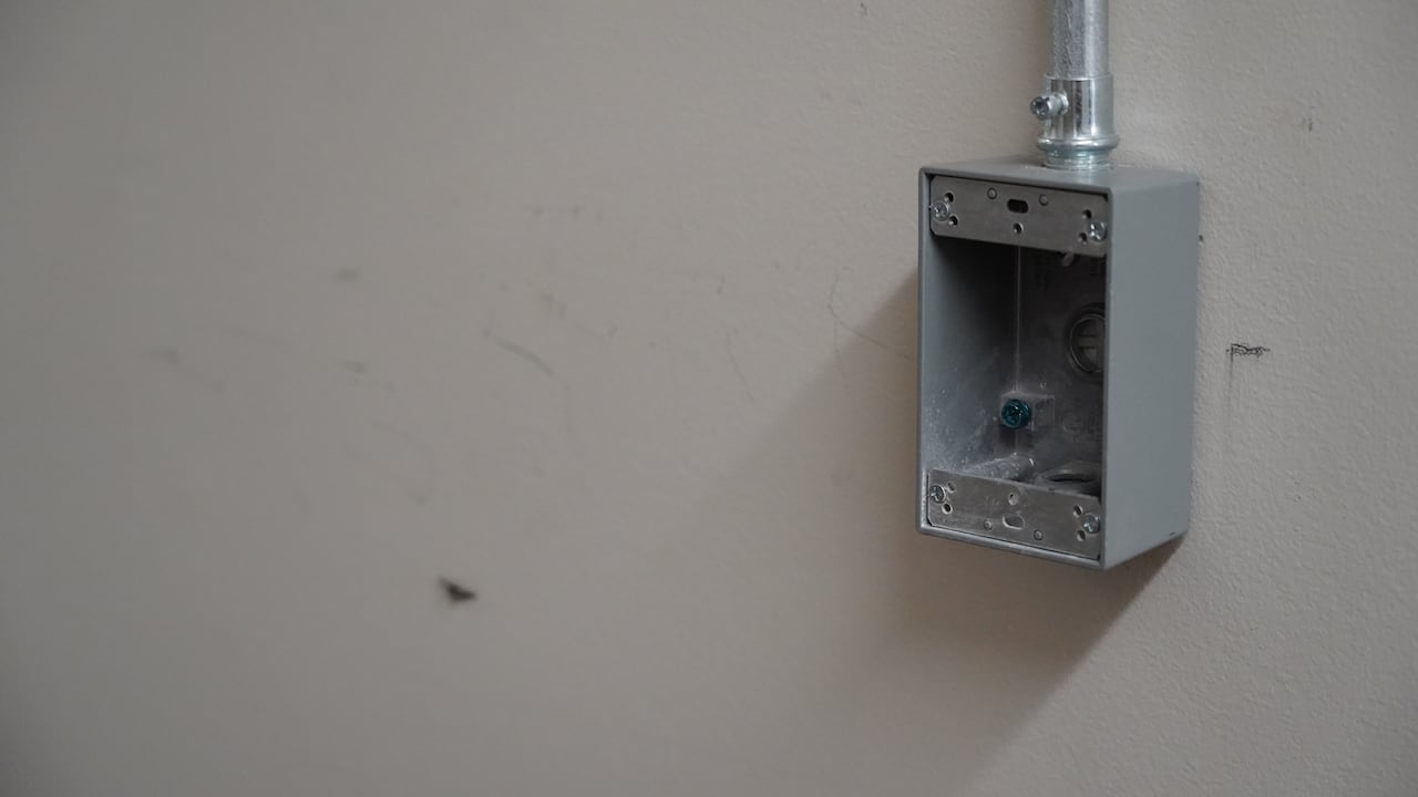 A close-up photo of a grey electrical box on a white wall that's scuffed and scratched.