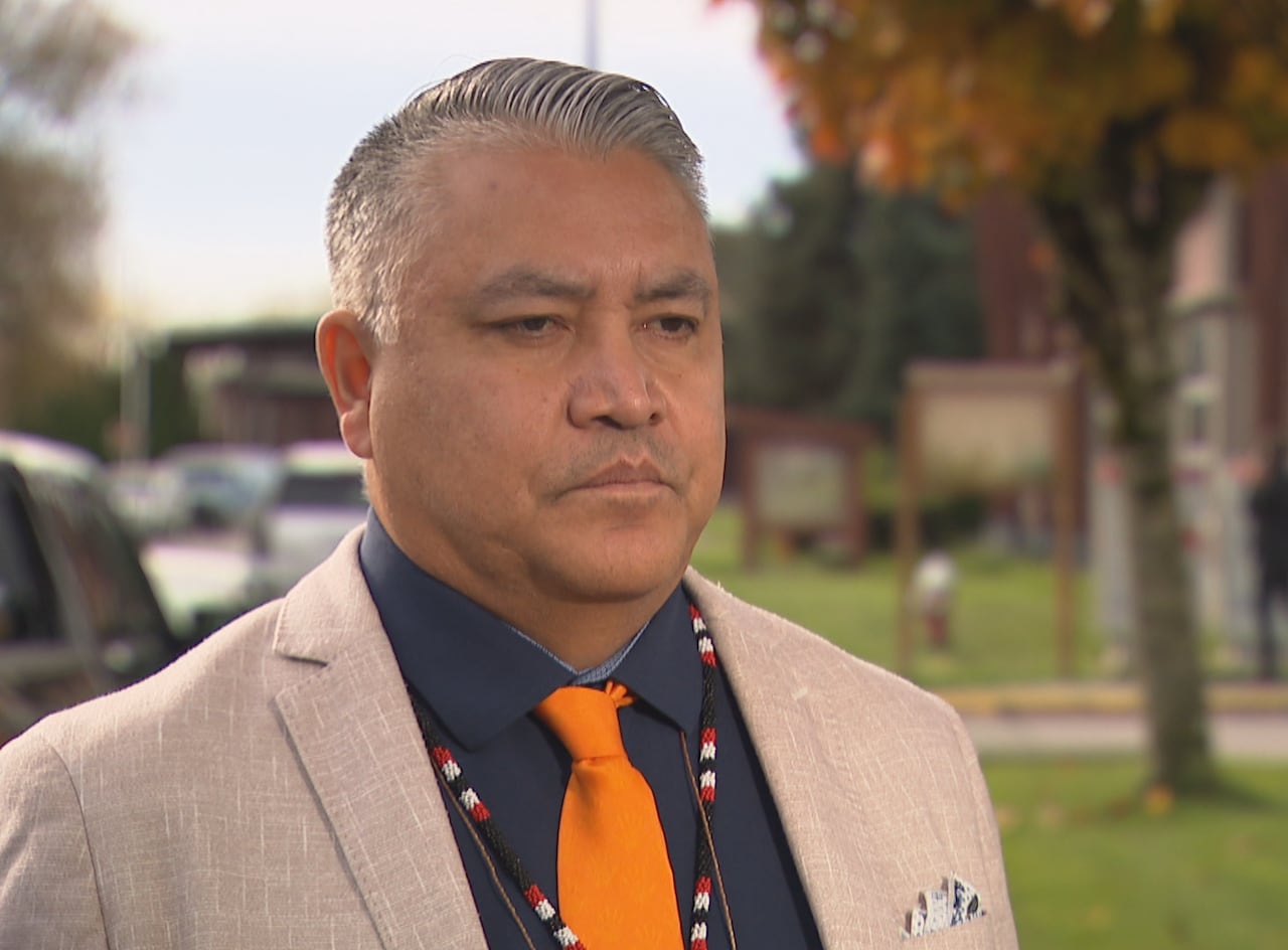 An Indigenous man wearing a cream-coloured jacket speaks outdoors.